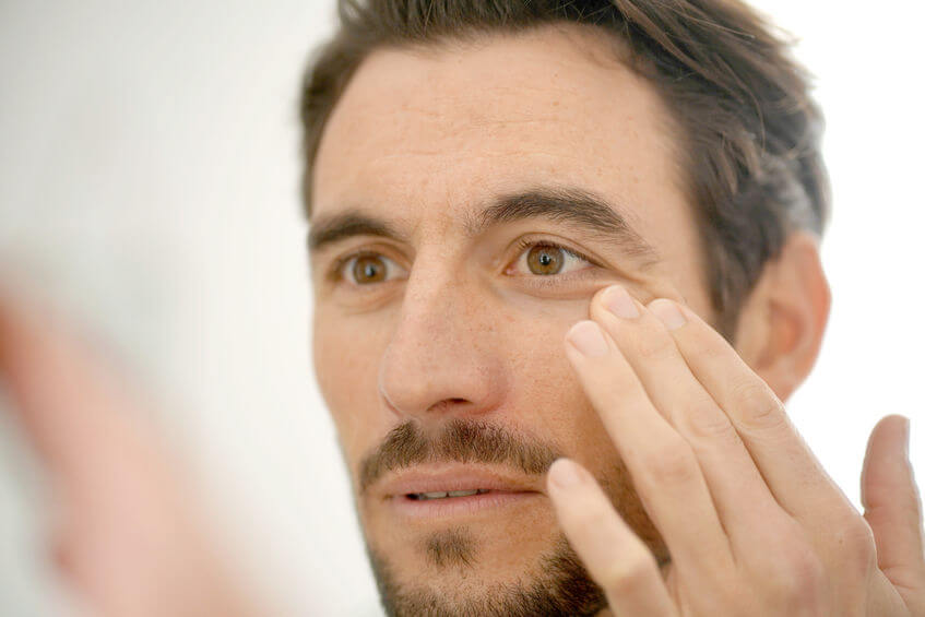 Handsome man checking wrinkles in mirror at home